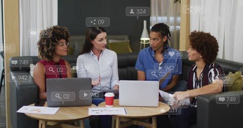 Collaborating team on sofa discussing social campaign with laptops and reaction icons