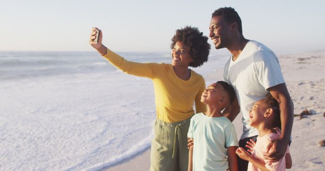 Smiling african american family taking selfie and embracing on sunny beach. healthy, active family beach holiday.