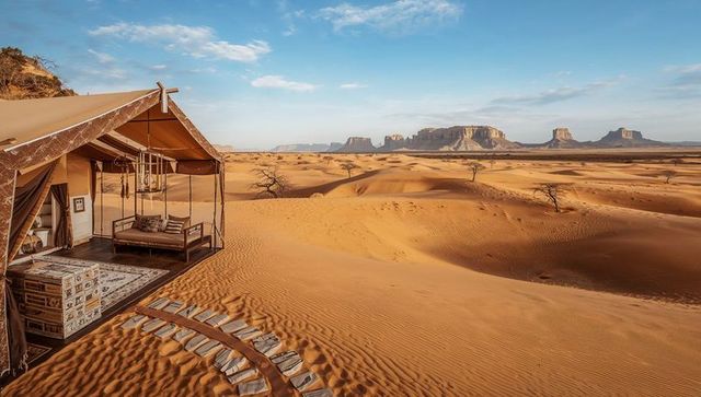 Luxury desert glamping tent overlooking sweeping sand dunes and sandstone buttes at golden hour