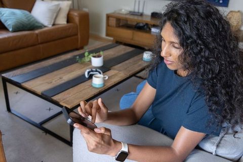 African american woman scrolling smartphone on couch wearing smartwatch cozy living room