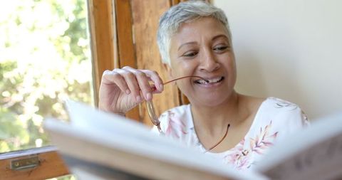 Happy Senior Woman Relaxed Reading by Window in Bright Home