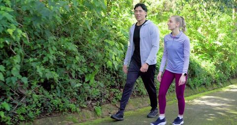 Young couple walking briskly on park trail in athletic wear checking smartwatch for fitness