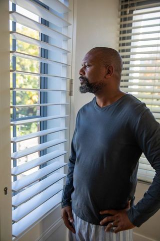 Mature african american man contemplating by sunlit window blinds showing wedding ring