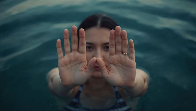 Swimmer reaching through teal water with open palms and ring, closeup portrait, calm mood