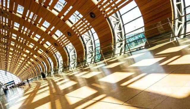 Sunlight streaming through vaulted wooden slats and arched skylights in transit concourse