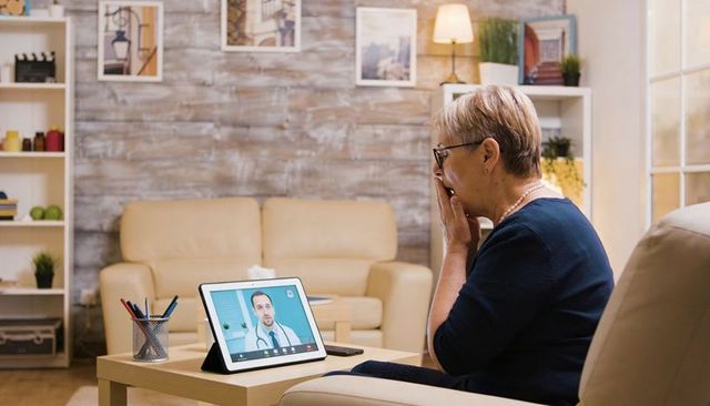 Senior woman using tablet for telehealth consultation with doctor in cozy living room