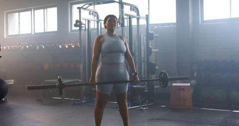 Woman lifting loaded barbell in commercial gym demonstrating strength, focus and disciplined trainin