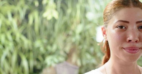 Young woman making eye contact in garden with soft green bokeh and calm expression