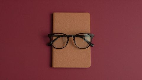 Minimalist brown notebook with black glasses on maroon background