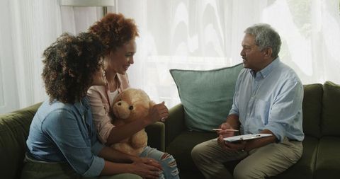 Multicultural women meeting senior counselor at home with teddy bear during family therapy