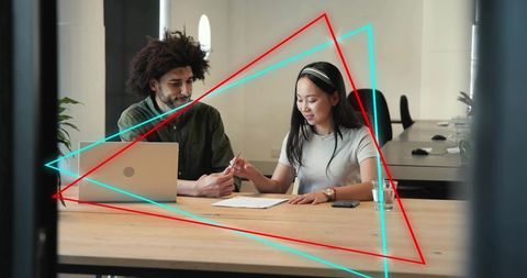 Colleagues reviewing document at coworking table with laptop and neon geometric overlays