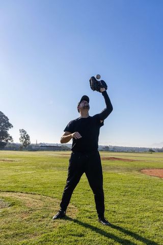 Mature man catching baseball with glove on sunny field during practice drill