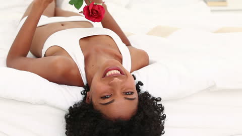 Joyful Woman Relaxing on Bed with Red Rose