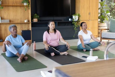 African american women practicing group meditation and gentle yoga in sunlit living room