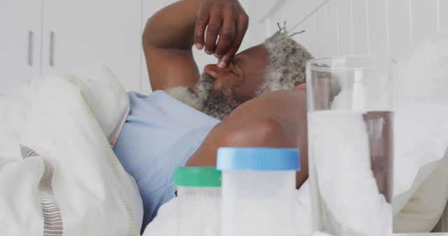Sick african american man in bed with medication containers on bedside table. Senior lifestyle, health domestic life, unaltered.