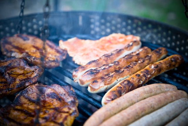 Close up view of a barbecue with grilled meats like chicken, pork chops and sausages. Perfect for use in cooking blogs, barbecue restaurant menus, outdoor party invitations, and summer grilling ads.