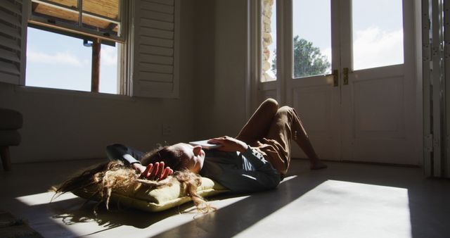 Caucasian woman lying on floor holding book and sleeping in sunny cottage living room. simple living in an off the grid rural home.