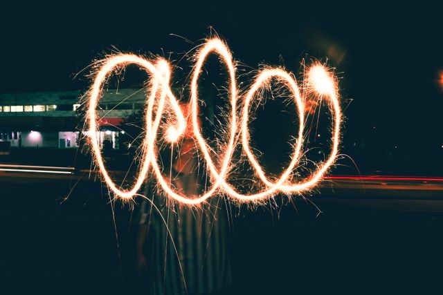 Person creating the word 'Cool' using a sparkler in a dark setting. This colorful light painting suggests fun and celebration. Great for advertising festive events, creative art promotions, and summer activities.