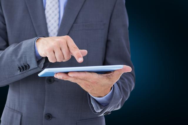 Businessman in a suit holding and using a digital tablet against a dark background. This image could be used for articles or advertisements related to technology in business, modern corporate settings, or innovative business solutions. Useful for depicting professional environments, digital transformation, and business technology communication.
