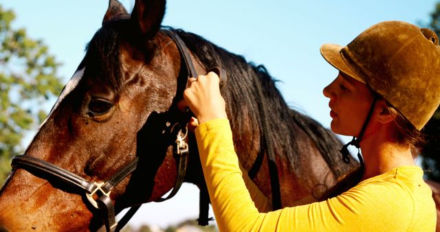 A young Caucasian woman wearing a riding helmet is affectionately grooming a horse, with copy space. Her gentle interaction with the animal suggests a bond and care for the horse's well-being.