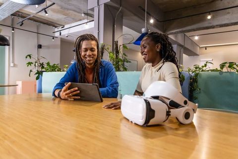 African-American coworkers collaborating with tablet and VR headset in modern coworking office