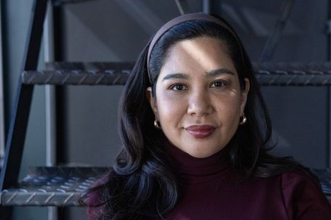 Sunlit asian woman sitting on industrial metal stairs wearing maroon turtleneck headband