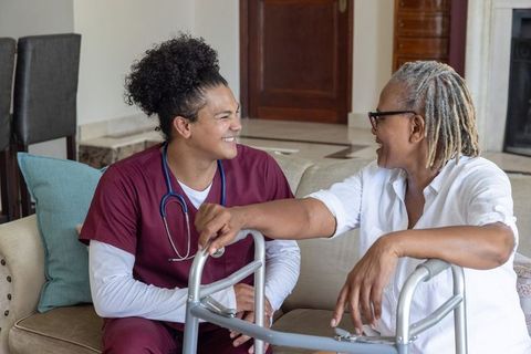Young male nurse providing friendly homecare to senior african-american woman using walker