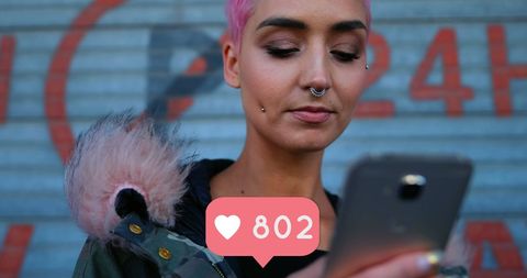 Trendy woman with pink hair using smartphone with social media like alert