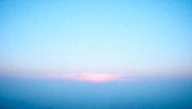 Pastel dawn horizon showing pale blue sky with pink cloud band over misty mountains