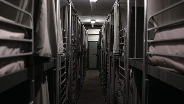 Narrow Dormitory Corridor Lined with Metal Bunk Beds and Curtains Under Dim Lighting