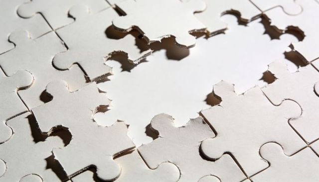 White torn jigsaw puzzle revealing central gap with rough edges and dramatic shadows
