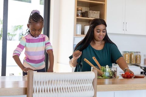 African american mom and daughter making fresh salad together in sunlit kitchen