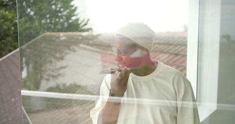 African man speaking into smartphone on balcony with reflective window and soft daylight