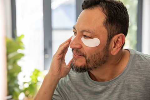 Mature asian man applying under-eye patches at vanity in sunlit interior