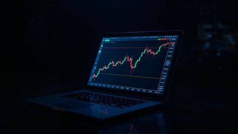 Laptop displaying online trading candlestick chart in dimly lit room