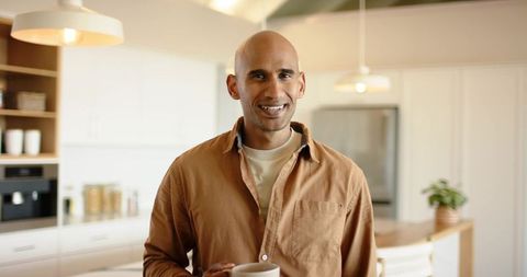 Indian man smiling in modern kitchen holding mug, cozy morning home lifestyle and wellness