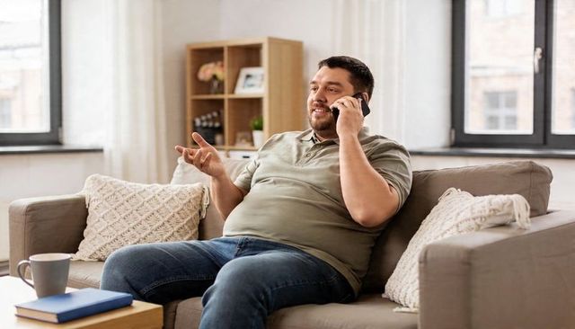 Bearded man talking on smartphone while gesturing and relaxing on cozy living room sofa