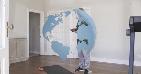 Chinese man holding tablet in home gym viewing holographic globe for fitness wearable tech