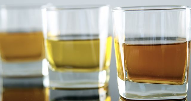 Glasses filled with amber-colored liquid, whiskey or scotch, are lined up on a reflective surface - Download Free Stock Photos Pikwizard.com