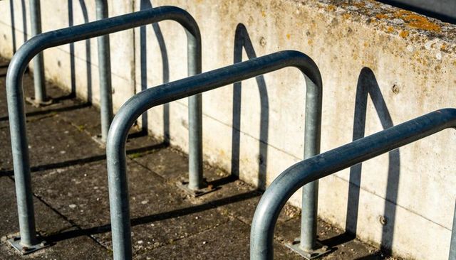 Galvanized u-shaped bike racks casting long curved shadows on concrete plaza wall