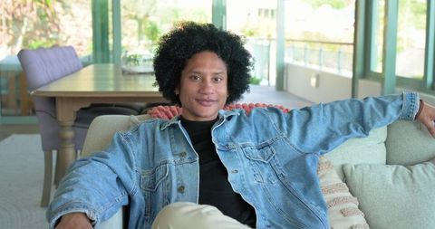 Relaxed african american man lounging on sofa in bright living room wearing denim jacket