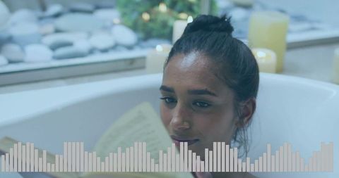 Woman relaxing in bathtub with book and candles