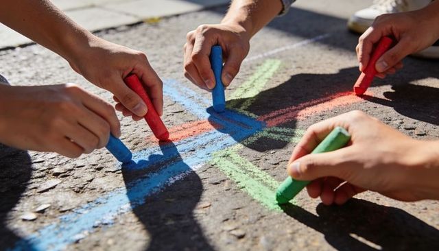 Adults drawing bright chalk lines on sunlit asphalt for community play and teamwork