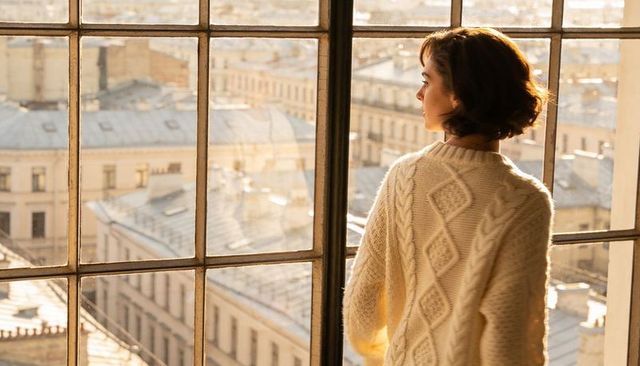 Woman wearing cream cable knit sweater gazing over city rooftops at golden hour