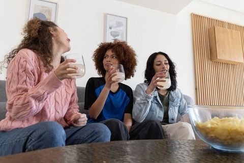 Friends sipping creamy drinks and sharing chips on couch during relaxed living room hangout
