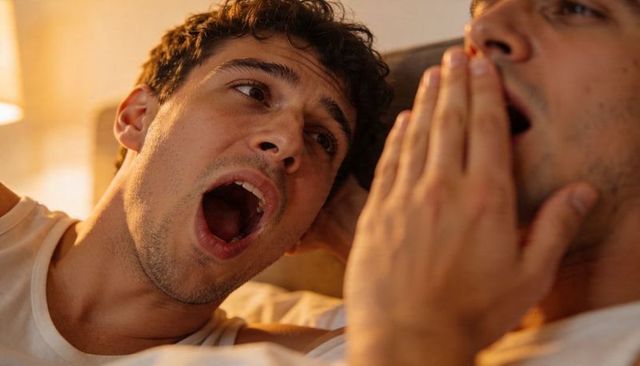 Yawning man reclining in bed during cozy evening with soft lamp light