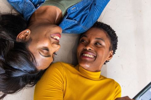 Diverse women lying head-to-head laughing and smiling with smartphone