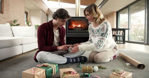 Cheerful friends wrapping gifts near cozy fireplace
