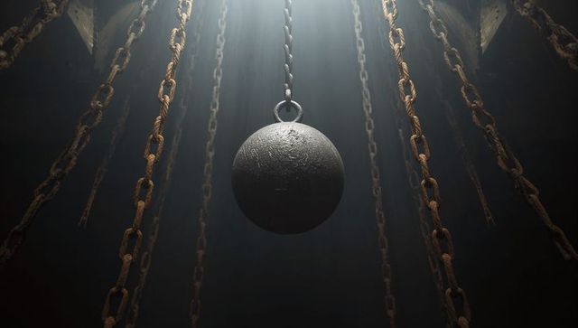Swinging wrecking ball suspended by rusted chains in industrial chamber, dramatic light
