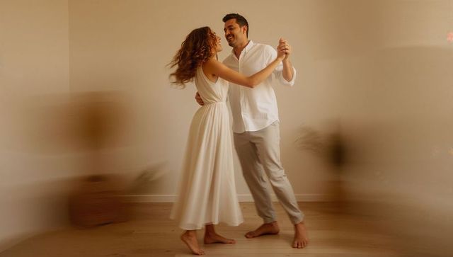 Barefoot couple twirling on warm wooden floor, flowing white dress and shirt, intimate